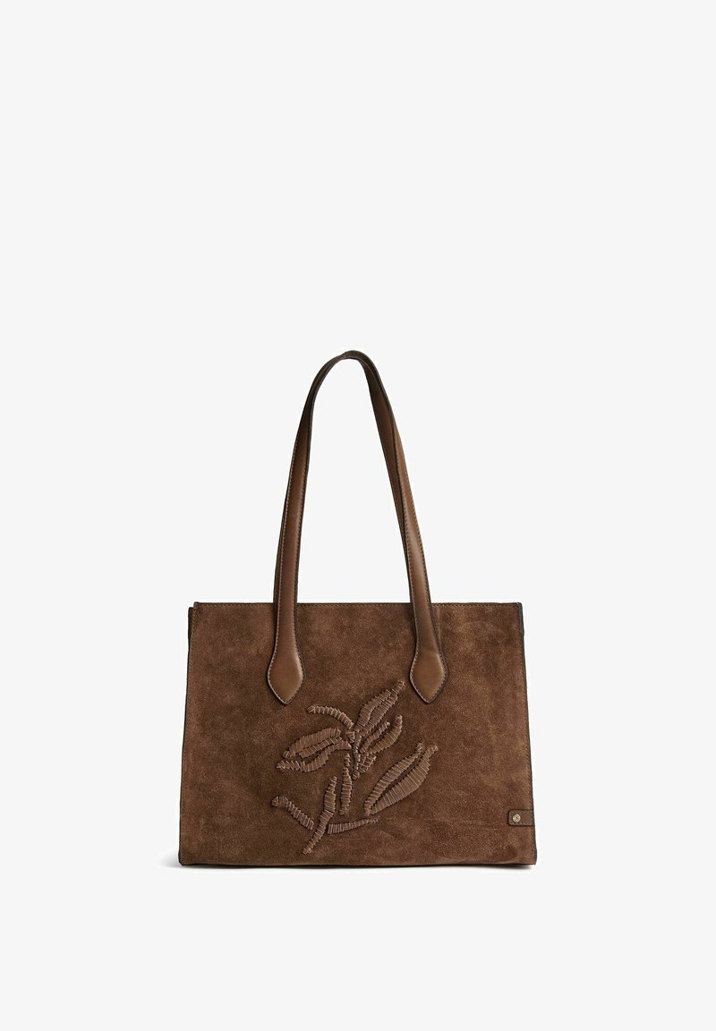 Sac cabas en daim marron avec deux anses en cuir et motif de feuille brodé sur le devant sur fond blanc.