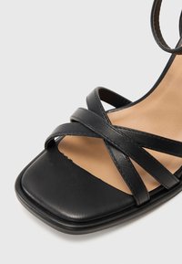 Sandale noire en cuir avec des brides croisées et une bride de cheville, dotée d'un carré ouvert à l'avant et d'une semelle intérieure beige.