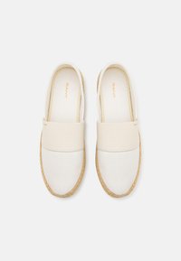 Paire d'espadrilles off-white sans lacets avec dessus en tissu et bordure de semelle en jute tissée, marquées "GANT" à l'intérieur et près de l'ouverture.