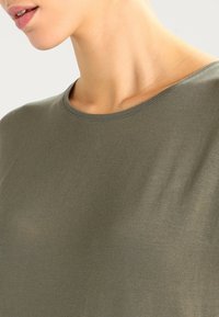 Olivkowy, krótko rękawowy T-shirt o gładkiej fakturze, zaokrąglonym dekolcie i delikatnym przeszyciu wzdłuż kołnierza.