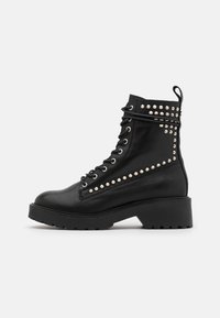 Czarne skórzane botki za kostkę z masywną podeszwą, metalowymi ćwiekami po bokach oraz tradycyjnym sznurowaniem i pętlą do zakładania z tyłu.