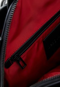 Czarna kieszeń na zamek błyskawiczny o g�ładkiej powierzchni, wewnątrz w jasnoczerwonym wykończeniu, z czarnym uchwytem zamka i starannym przeszyciem wzdłuż krawędzi.