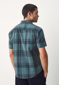 Kortærmet ternet skjorte i teal med grønne og lilla striber, med knaplukket krave og tekstureret stof. Set bagfra.