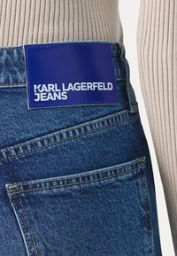 Traperice s plavom umjetnom kožnom oznakom s natpisom "KARL LAGERFELD JEANS". Karakteristično šivanje i klasični dizajn s pet džepova.