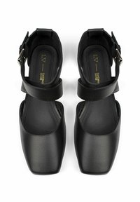 Sandale negre din piele cu un design cu vârf pătrat, dotate cu bretele ajustabile pentru gleznă și o textură netedă. Talpa este plată și minimală.