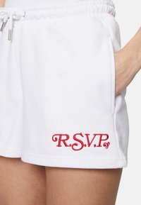 Shorts blancos confeccionados en tela suave con cintura elástica, que presentan un detalle bordado en rojo de "R.S.V.P." en el lado inferior izquierdo.