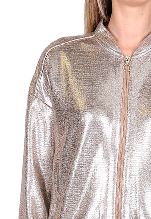 Metalen bomberjack in lichtgoud. Beschikt over een hoge kraag, een ritssluiting aan de voorkant en een gladde, glanzende textuur. Geen zichtbare patronen of accenten.