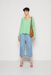 Grønn bluse med blomstermønster og V-hals, kombinert med en lys blå denimskjørt med en frontslisse. Brun skulderveske og beige sandaler.