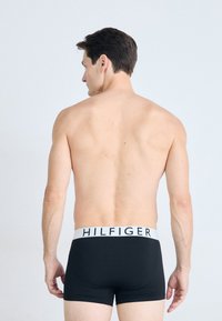 Schwarze Boxer-Briefs mit einem weißen elastischen Bund, der das "HILFIGER"-Logo trägt. Glatte Textur, eng anliegendes Design, von hinten betrachtet.