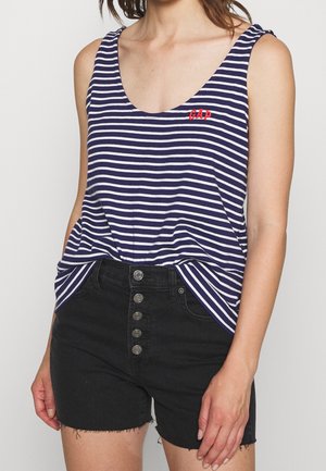 Femme portant un top sans manches rayé bleu marine et blanc avec un logo rouge "GAP" et un short en denim noir taille haute avec cinq boutons sur le devant.