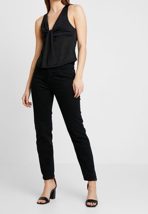 Sort ærmeløs top med en knyttet front, parret med tætsiddende sorte jeans og sorte hælede sandaler; glat stof og skræddersyet pasform.