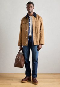 Jachetă din pânză maro cu guler bleumarin, cu închidere prin nasturi, patru buzunare. Cămașă albă, blugi din denim albastru, pantofi din piele maro și o geantă din piele.