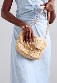 Υφασμένη τσάντα χιαστί από ψάθα σε μπεζ χρώμα με φρουτοσαλάτα, διαθέτει χρυσό κούμπωμα και αλυσίδα για τιράντα. Ομαλή φόρεμα από ύφασμα σε ανοιχτό μπλέ.