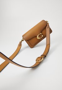 Brown leather handbag with a gold hardware clasp, rectangular shape, adjustable strap, smooth texture, and simple design.