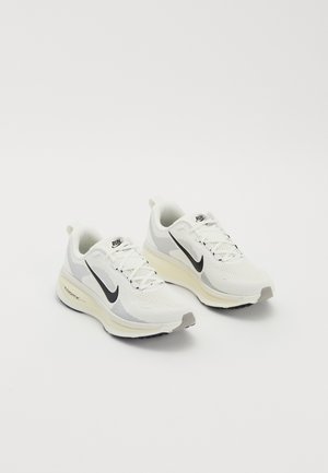 Pair of white running shoes with black Nike swoosh logos, cushioned soles, and laces, positioned on a plain white background.