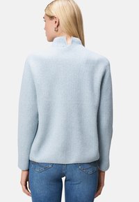 Helles blaues geripptes Sweatshirt mit hohem Kragen und einem Schlitzdetails auf der Rückseite. Weicher Stoff und lange Ärmel, kombiniert mit eng anliegenden blauen Jeans.
