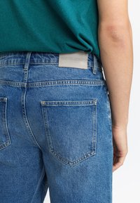 Blauwe denim jeans met een relaxte pasvorm, voorzien van een lichte wassing, twee achterzakken en een grijze leren label met de tekst "RE/VOLUTION."