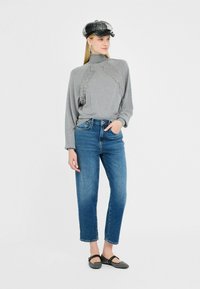 Top gris de manga larga con detalles texturizados, jeans azules de cintura alta y gorra de cuadros negros, complementado con zapatos planos negros.