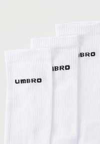 Calzini bianchi in cotone con trama a coste, con logo "UMBRO" nero stampato sui lati. Tre paia impilati.