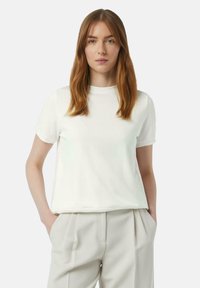 White short-sleeve t-shirt made of soft cotton fabric. Features a round neckline and a relaxed fit, paired with light beige pleated trousers.