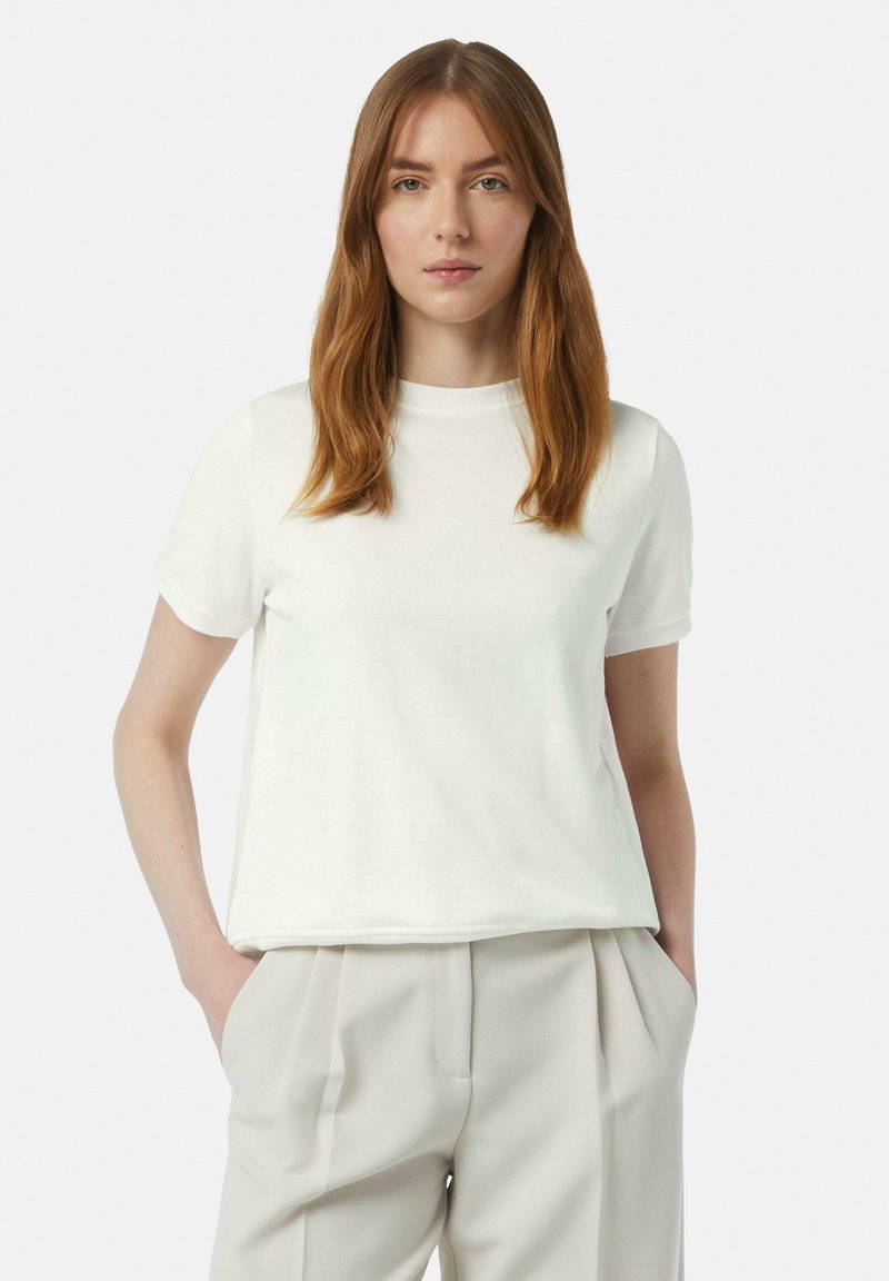 White short-sleeve t-shirt made of soft cotton fabric. Features a round neckline and a relaxed fit, paired with light beige pleated trousers.