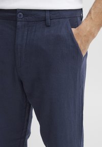 Pantaloni din in bleu închis, cu croi lejer, cu închidere frontală cu buton, buzunare laterale și textura moale.