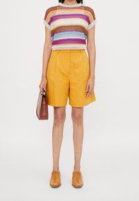 Top de punto a rayas en azul, rosa y amarillo con mangas cortas; pantalones cortos amarillos a medida; bolso marrón; zapatos de tela color beige.