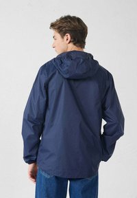 Marineblaue wasserdichte Jacke mit Kapuze, elastischen Bündchen und lockerem Schnitt. Glatte Textur, leichtes Material und schlichtes Design.