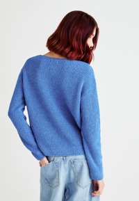 Blå strikket genser med avslappet passform, med ribbestruktur og lange ermer, sammen med lyseblå denimjeans.