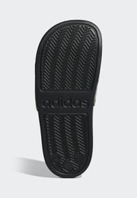 Czarna gumowa podeszwa do butów z wzorem jodełki. Zawiera wytłoczoną nazwę marki "adidas" oraz rozmiar "12" w pobliżu pięty. Gładka tekstura na całej powierzchni.