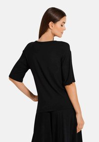 Zwarte korte mouwen top met een losse pasvorm en een ronde halslijn. Glad textuur met een minimalistisch ontwerp, met een rechte snit aan de zoom.