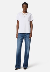 White cotton t-shirt with a round neckline and gold logo, paired with light blue wide-leg jeans and pointed black heels.