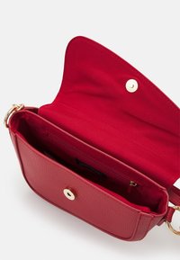 Červená texturovaná kožená crossbody taška s otevřeným vrchem, s zlatými kovovými detaily a malou vnitřní zipovou kapsou. Interiér je podšitý červenou tkaninou.