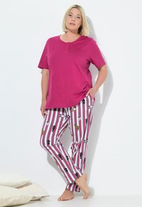 Różowy top z krótkim rękawem z trzema guzikami, w połączeniu z białymi wzorzystymi spodniami w paski, ozdobionymi ilustracjami psów w różnych kolorach.