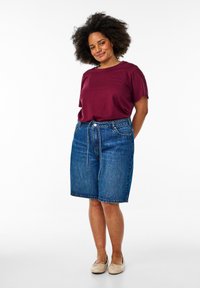 T-shirt bordeaux à manches courtes associé à un short en denim bleu, avec une taille à cordon de serrage et des ourlets retroussés. Porté avec des ballerines beiges.