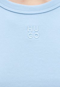 Ανοιχτό γαλάζιο ριμπ ύφασμα με ανάγλυφο κέντημα των γραμμάτων "HUGO" σε λευκό, κεντραρισμένο κοντά στον γιακά.