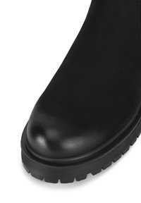 Černá bota se strukturovaným semišovým svrškem, kulatou špičkou a silnou gumovou podrážkou se zlomeným vzorem. Hladký povrch kožených detailů.