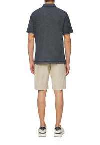 Kurzarmhemd in Marineblau mit strukturiertem Stoff und Kragen, kombiniert mit beigen Shorts und weißen Sneakers mit dunklen Akzenten.