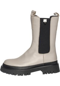 Bota de cuero beige hasta el tobillo con elástico negro en el lateral, suela negra resistente y tira para tirar. Presenta costuras a lo largo de la puntera y acabado liso.