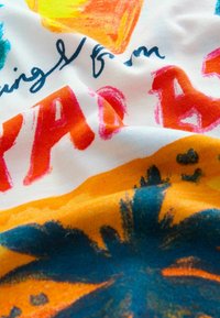 Katoenen stof met een witte achtergrond, voorzien van levendige oranje, roze en turquoise afbeeldingen, waaronder tropische motieven en handgeschreven tekst.