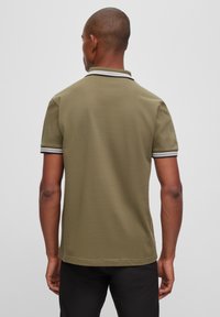Polo vert olive à manches courtes, avec un col à rayures noires et blanches contrastantes. Tissu lisse et texturé, coupe ajustée.