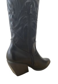 Botte noire en cuir montant jusqu'au genou, dotée d'une fermeture éclair sur le côté, de coutures décoratives, d'un bout pointu et d'un talon épais. Fini lisse avec des accents texturés.
