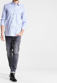 Světlomodrá kostkovaná košile s dlouhými rukávy, černými knoflíky, doplněná tmavě šedými džíny a černými kotníkovými botami. Jednoduchý, střih na míru.