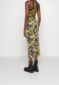 Svart linne med gul och vit barockmönster, kombinerat med en midjekort kjol med liknande design; svarta ankelboots med metalldetaljer.