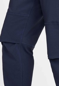 Marineblauwe sportbroek met een zachte textuur, dubbel gelaagd ontwerp en contrasterende stiksels, voorzien van meerdere zakdetails.