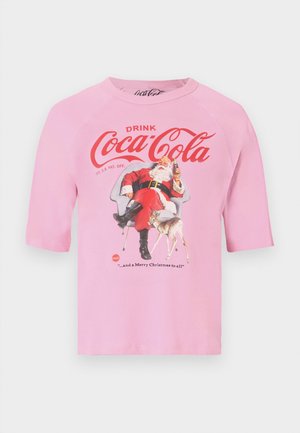 Rózsaszín ing vintage Coca-Cola logóval, a Mikulás egy széken ülve egy palackot tart a kezében, mellette egy kicsi szarvas.