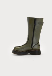 Bottes en cuir vertes jusqu'au genou avec fermetures éclair latérales, bord noir, semelle texturée et détail de couture orange contrastant. Design robuste avec un bout rond.
