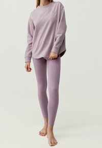 Violetti huppari, jossa on ribbireunat hihansuissa ja helmassa; yhdistetty matching-sovittaviin legginsseihin. Silkkinen kangas, minimalistinen muotoilu, ei näkyviä kuvioita tai koristeita.