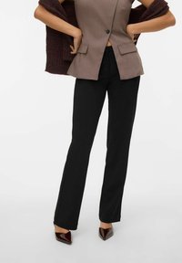 Blazer marrone attillato con due tasche frontali, abbinato a pantaloni neri a campana e tacchi a punta bordeaux, che offre un aspetto elegante e sartoriale.