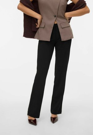 Blazer marrón ajustado con dos bolsillos frontales, combinado con pantalones de campana negros y tacones burgundy de punta, presentando un look elegante y a medida.